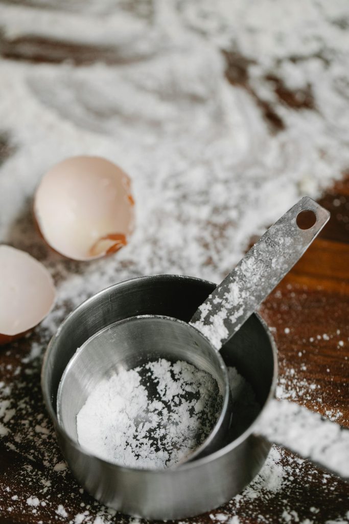 From above of stainless saucepans with eggshells on table with flour during cooking process